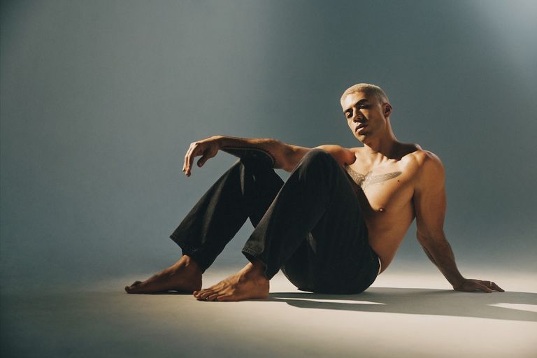 Promotional portrait of soul singer TEEKS sitting shirtless in black jeans against a studio backdrop, shot by photographer Frances Carter.